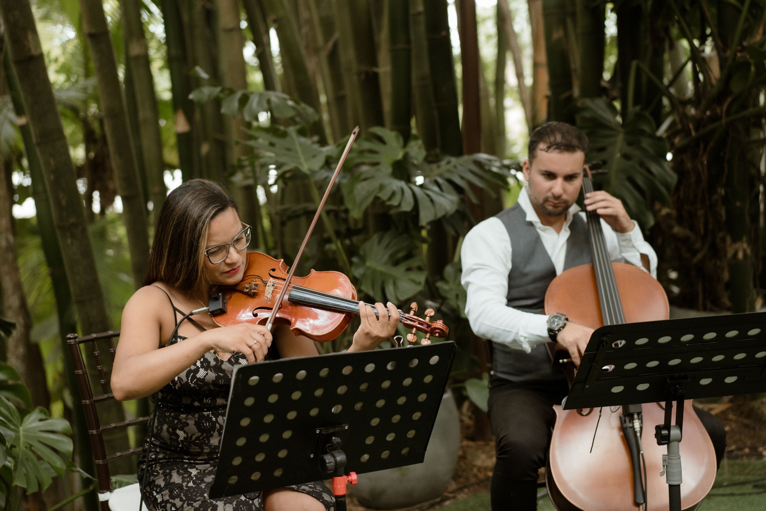 Musicians perform on violin and cello during an outdoor forest wedding ceremony.