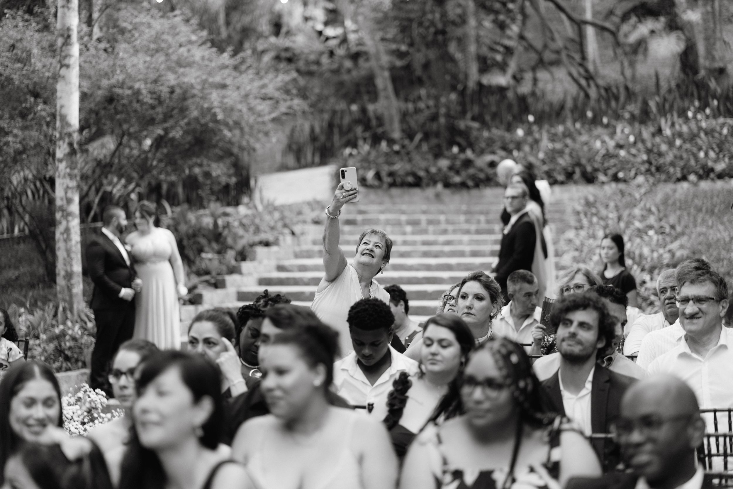 Black and white photo of wedding guests celebrating with raised arms in outdoor garden amphitheater.