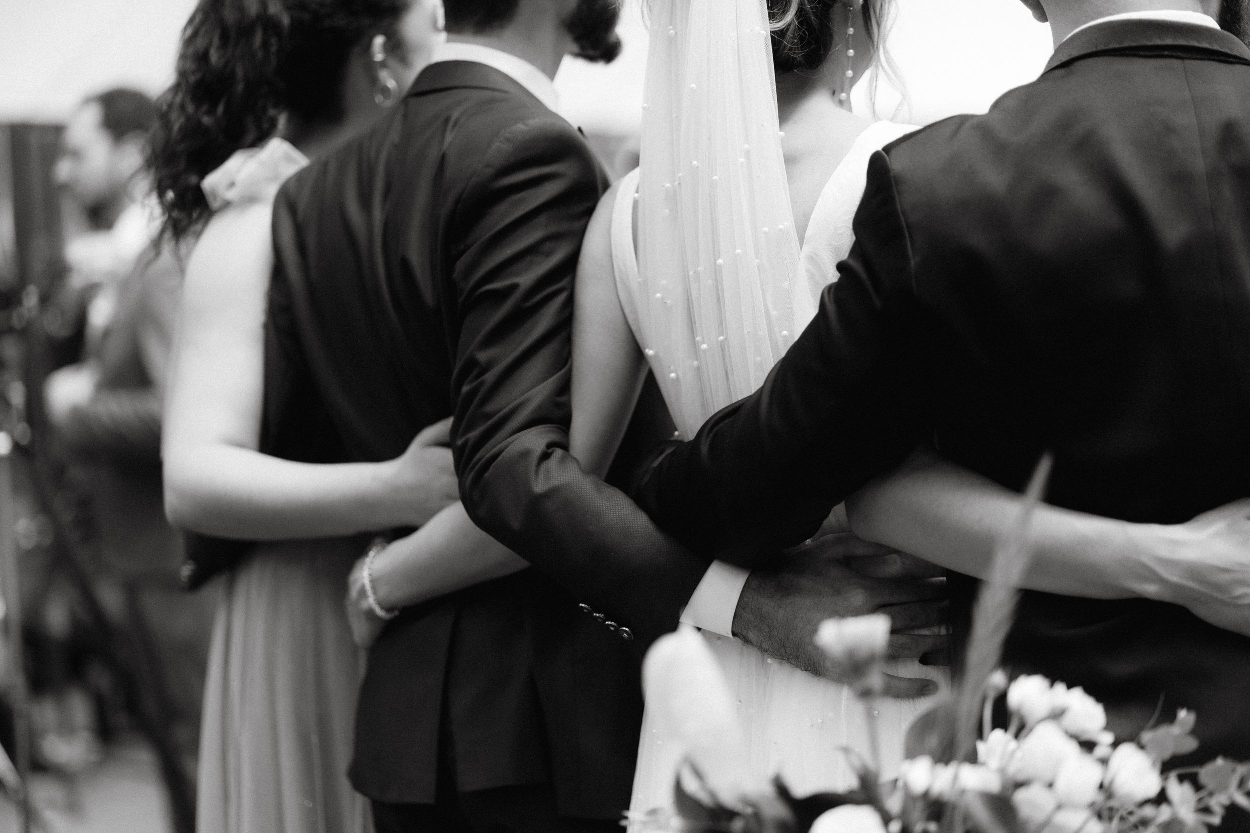 Intimate black and white photo showing wedding party embrace during celebration.