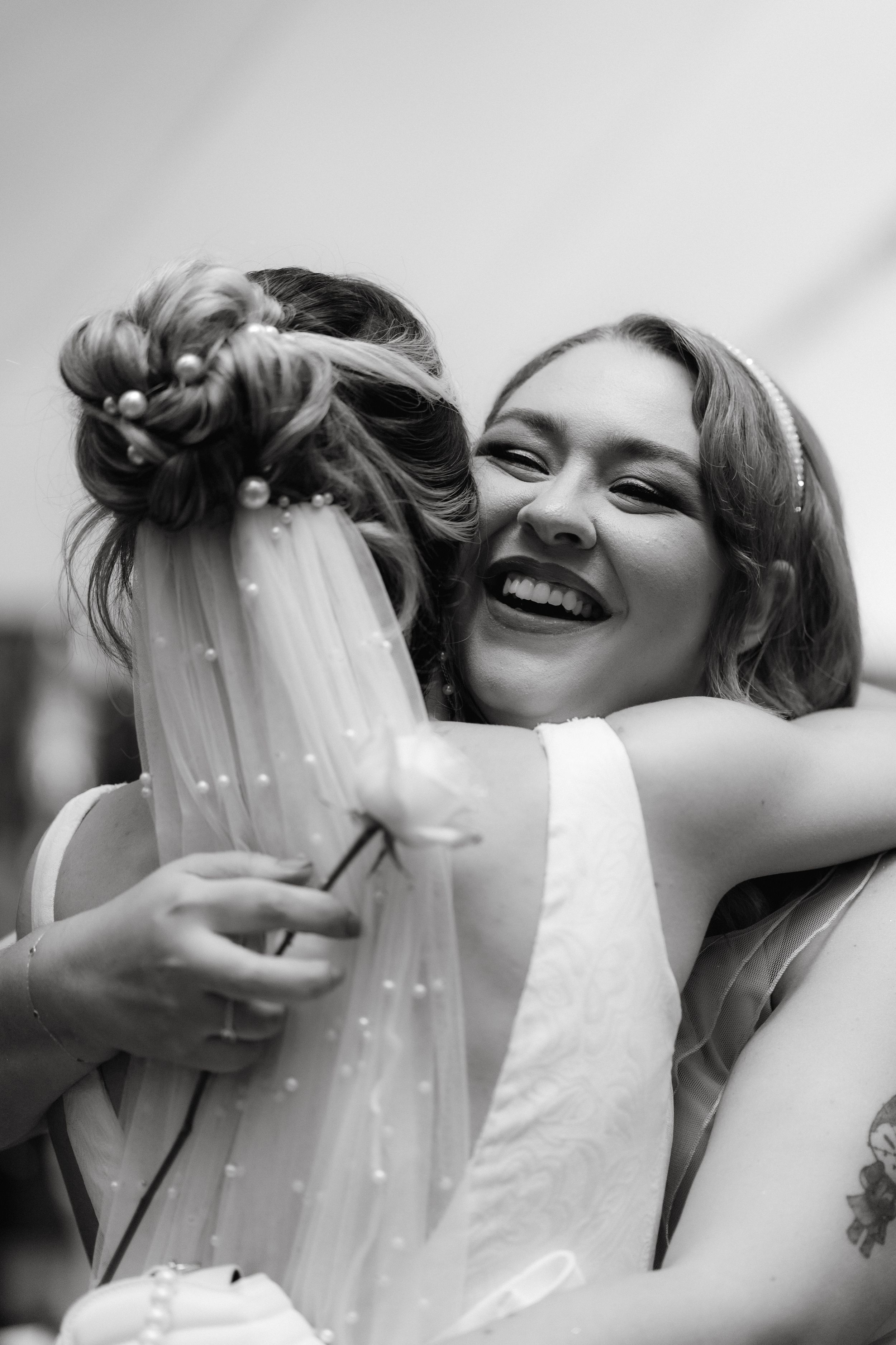 Black and white closeup of joyful celebratory hug with pearl-adorned veil.