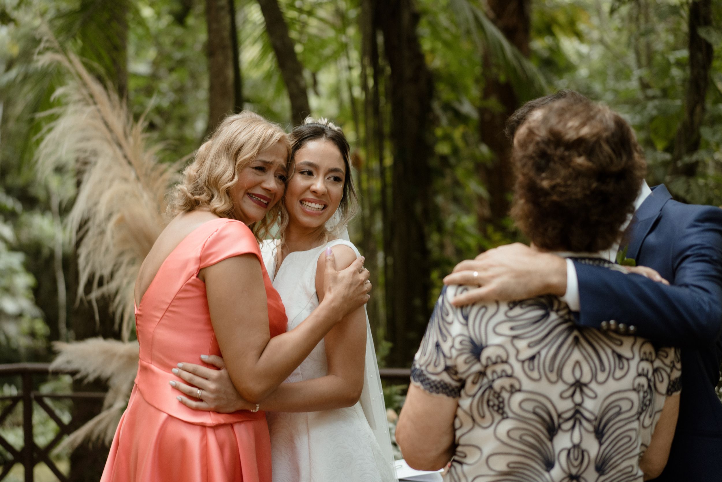 Emotional wedding celebration with bridal party embracing in sunlit forest setting.