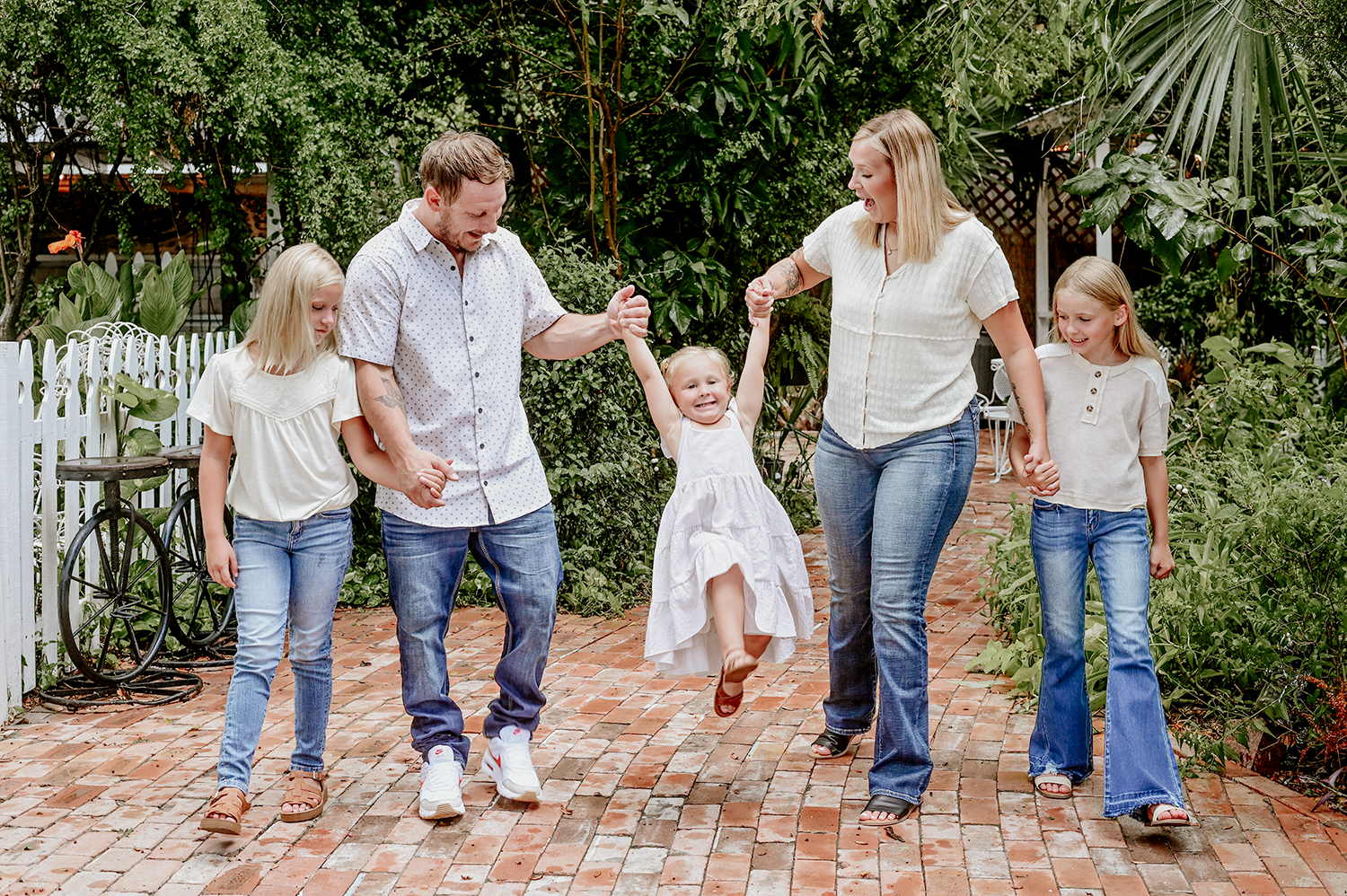 A family holds hands and laughs while walking together on a brick path.