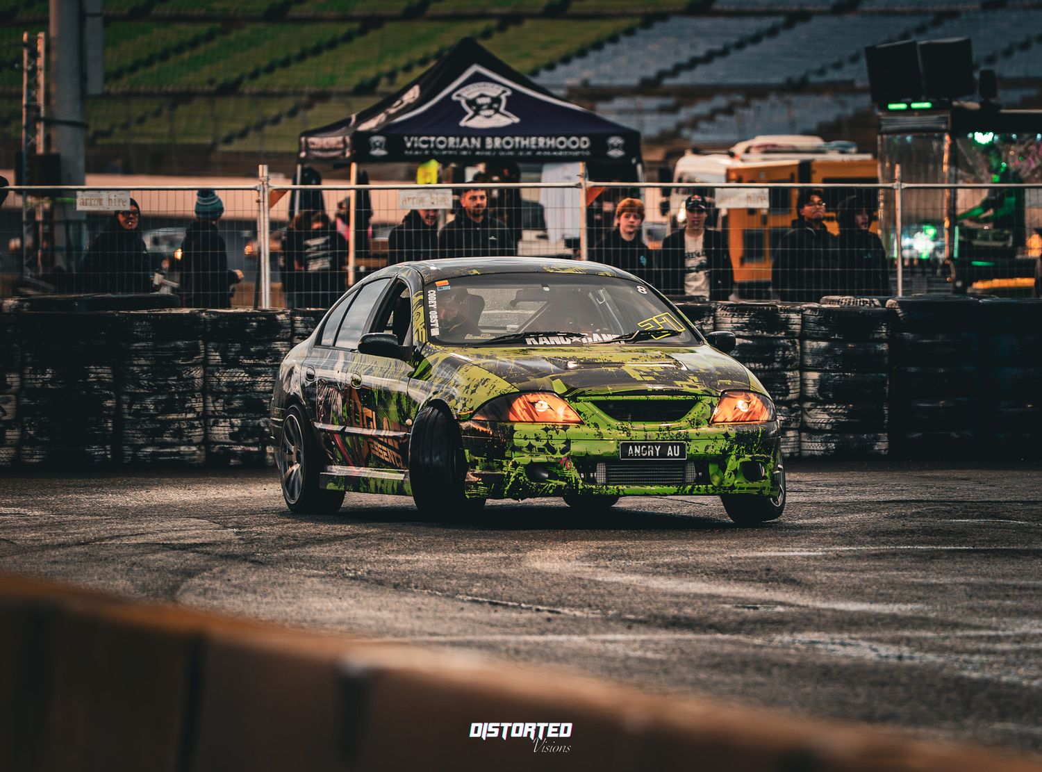 Green and yellow race car drifts across damp track surface at sunset.