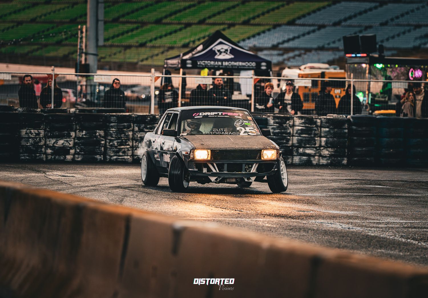 Modified silver sports car performs aggressive drift maneuver on darkened racing circuit.