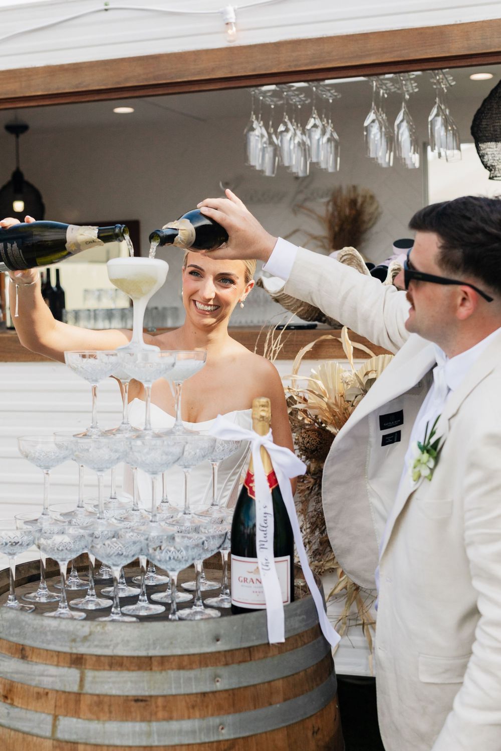 Bartenders in white uniforms arrange wine glasses on rustic wooden barrel bars at an elegant event.