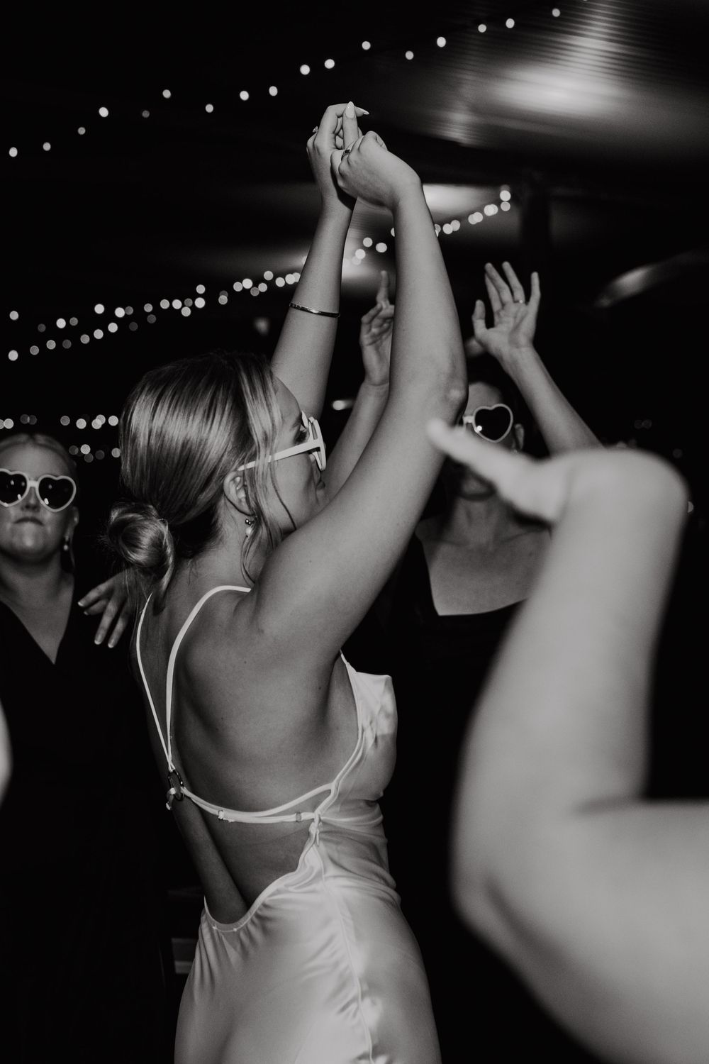 Black and white photos of people dancing at a party with string lights overhead creating a festive atmosphere.