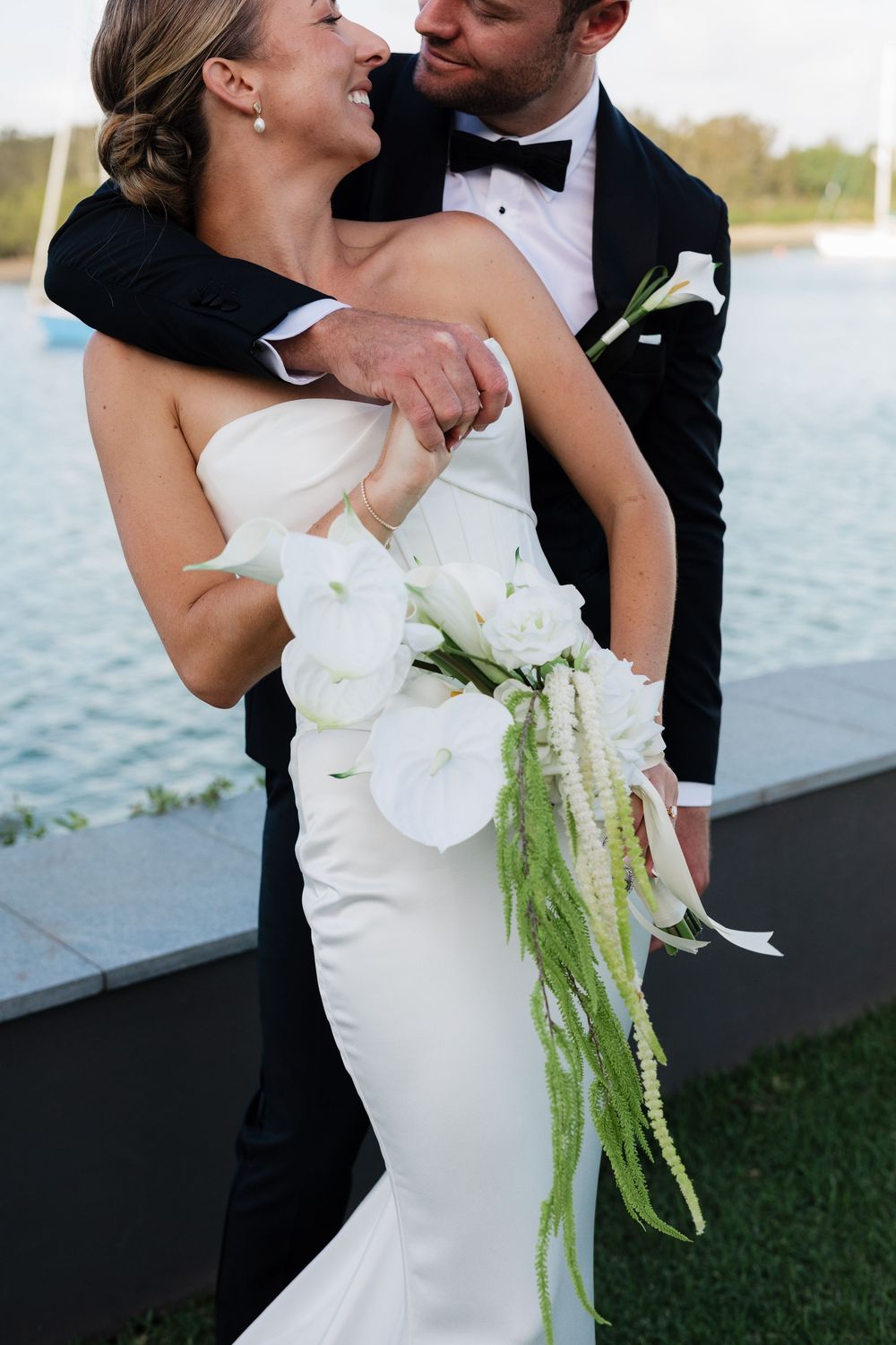 Newlyweds share intimate moments by the waterfront in a series of romantic wedding photos with white floral bouquet.