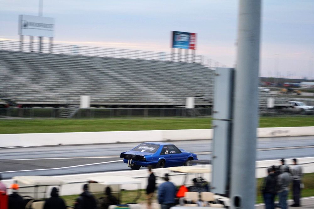 Blue drag racing car speeding down a racetrack with spectators watching from the stands.