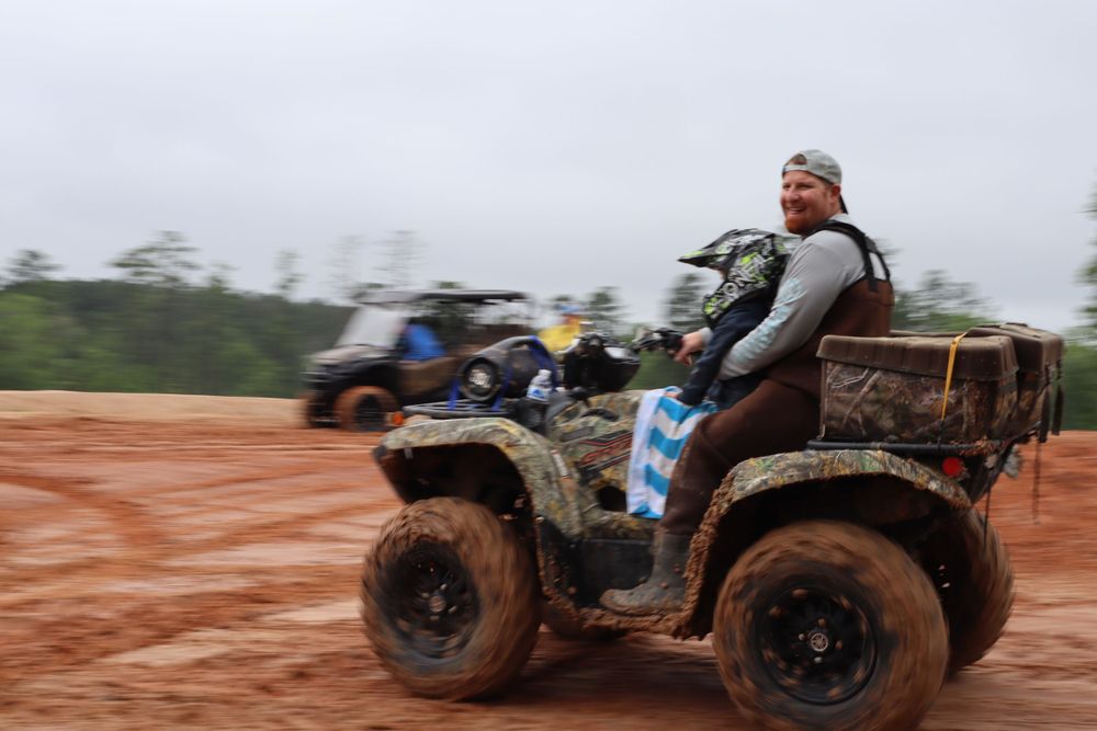 ATV rider speeds through muddy terrain on a cloudy day.