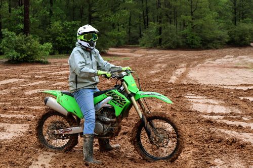 Green dirt bike rider navigating through a muddy off-road trail.