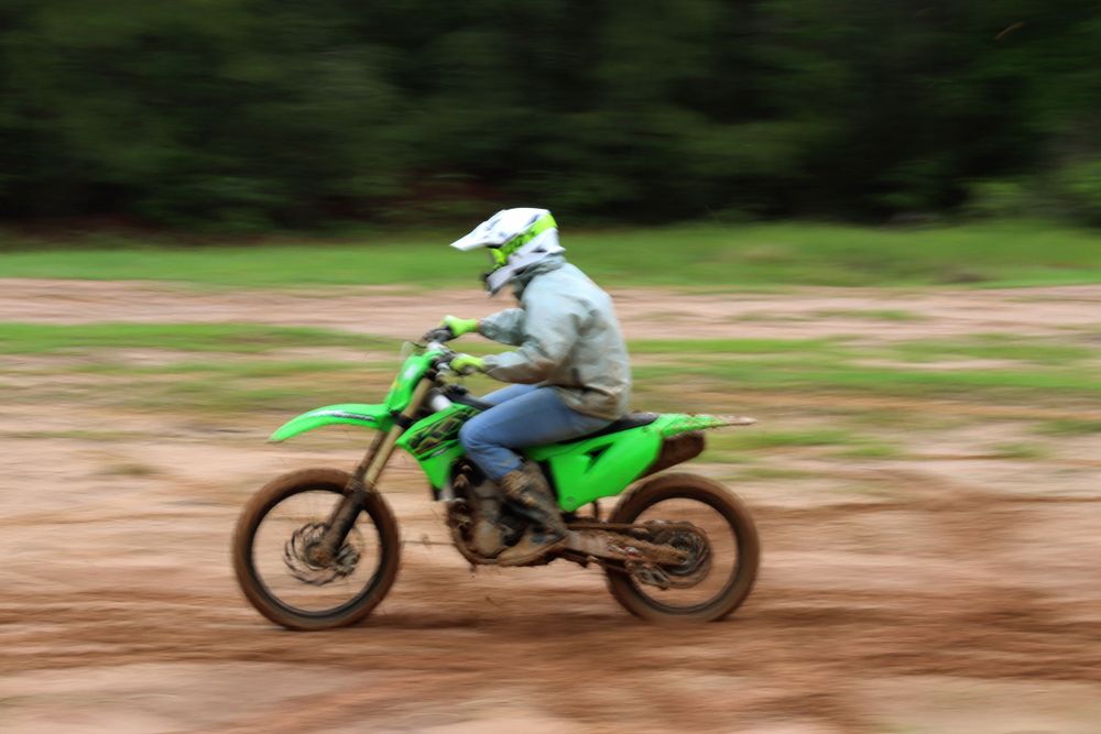 Motocross rider on green dirt bike creates motion blur while racing on dirt track.