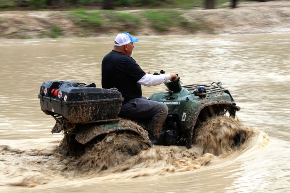 ATVs splash through deep muddy water crossing on an off-road trail.