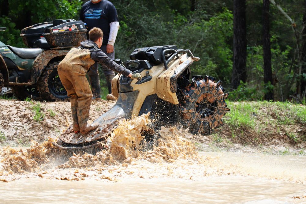 Off-road vehicles kick up mud and water while crossing a challenging water feature.