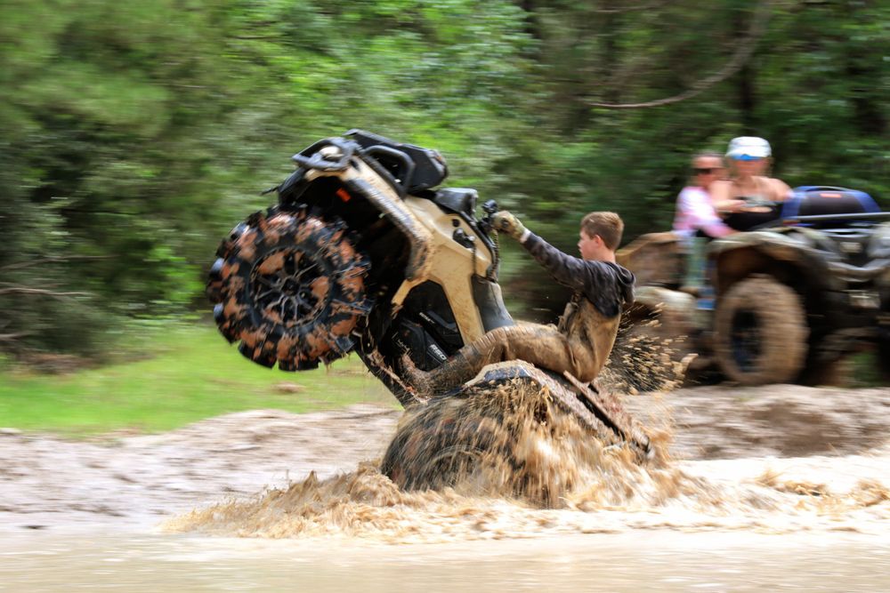 Dirt bikes kicking up mud while racing through a forest trail.