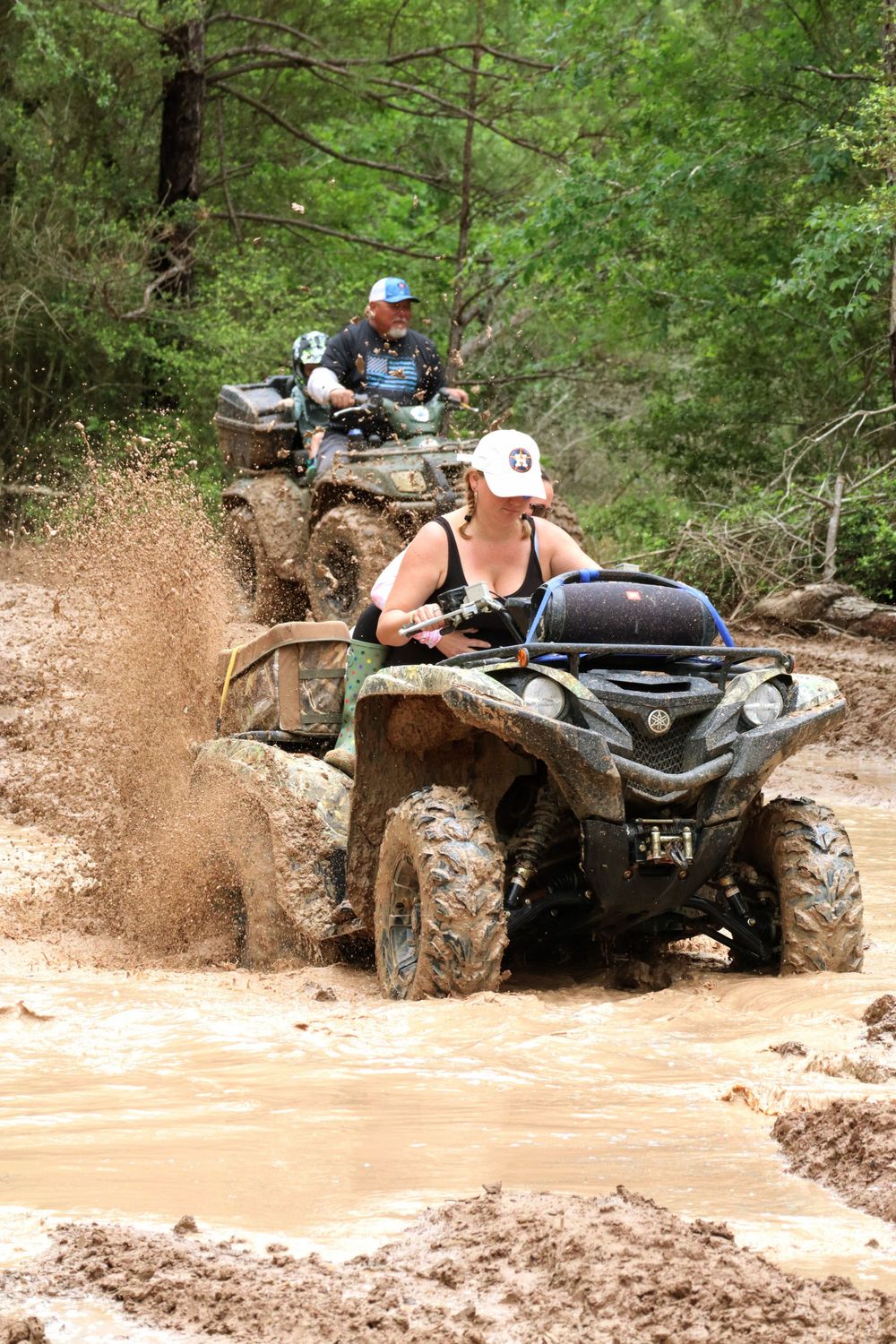ATVs splash through brown muddy water on an off-road trail.