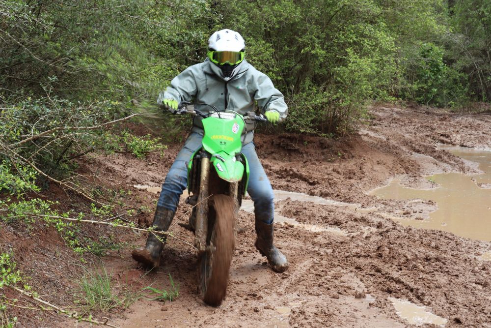 Off-road vehicles tackle a muddy trail section in the woods.