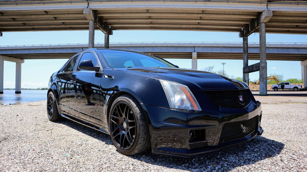 Black Cadillac CTS-V sedan with custom black wheels parked under a covered structure.