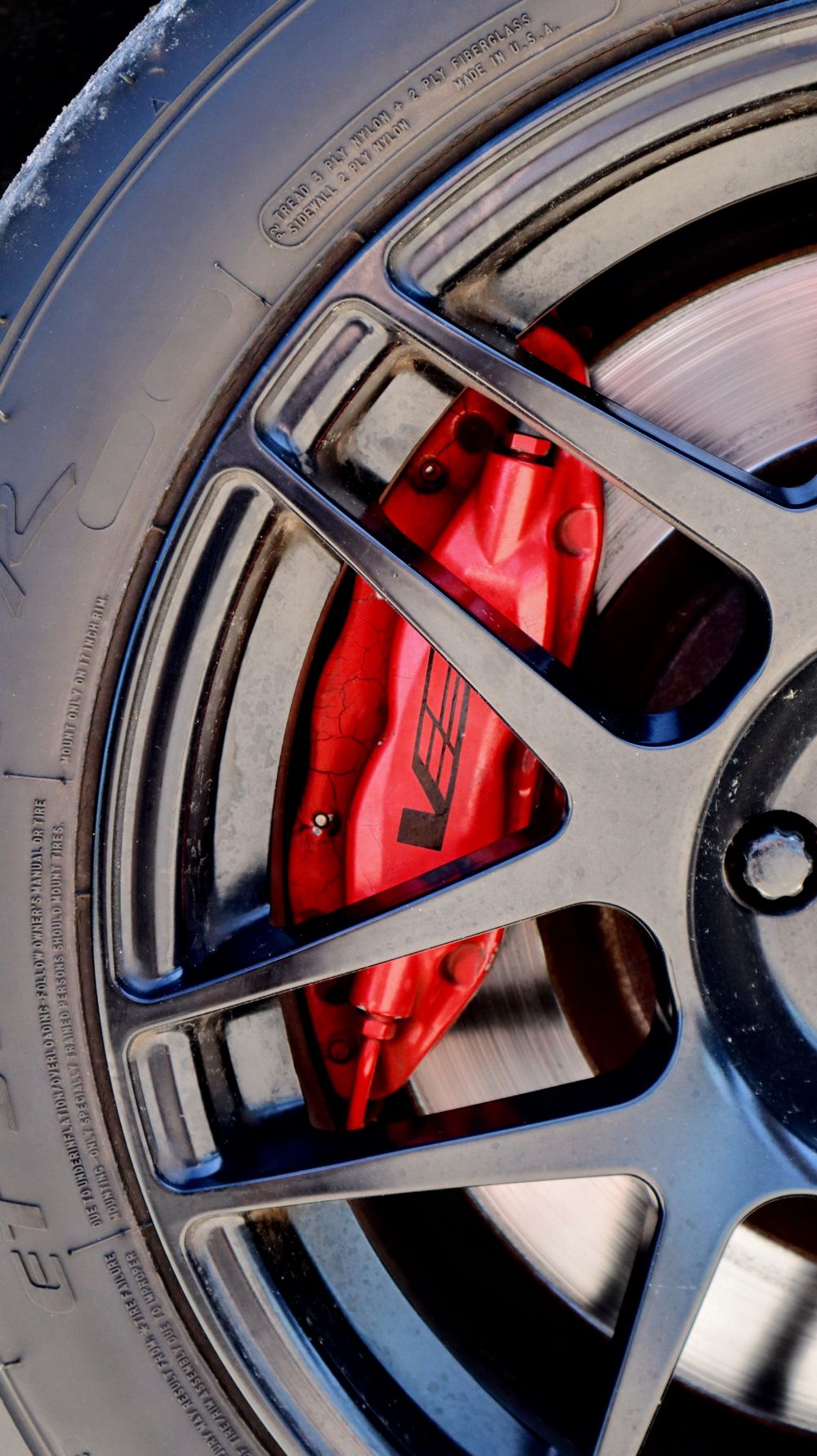 Close-up of a red performance brake caliper visible through a silver alloy wheel.