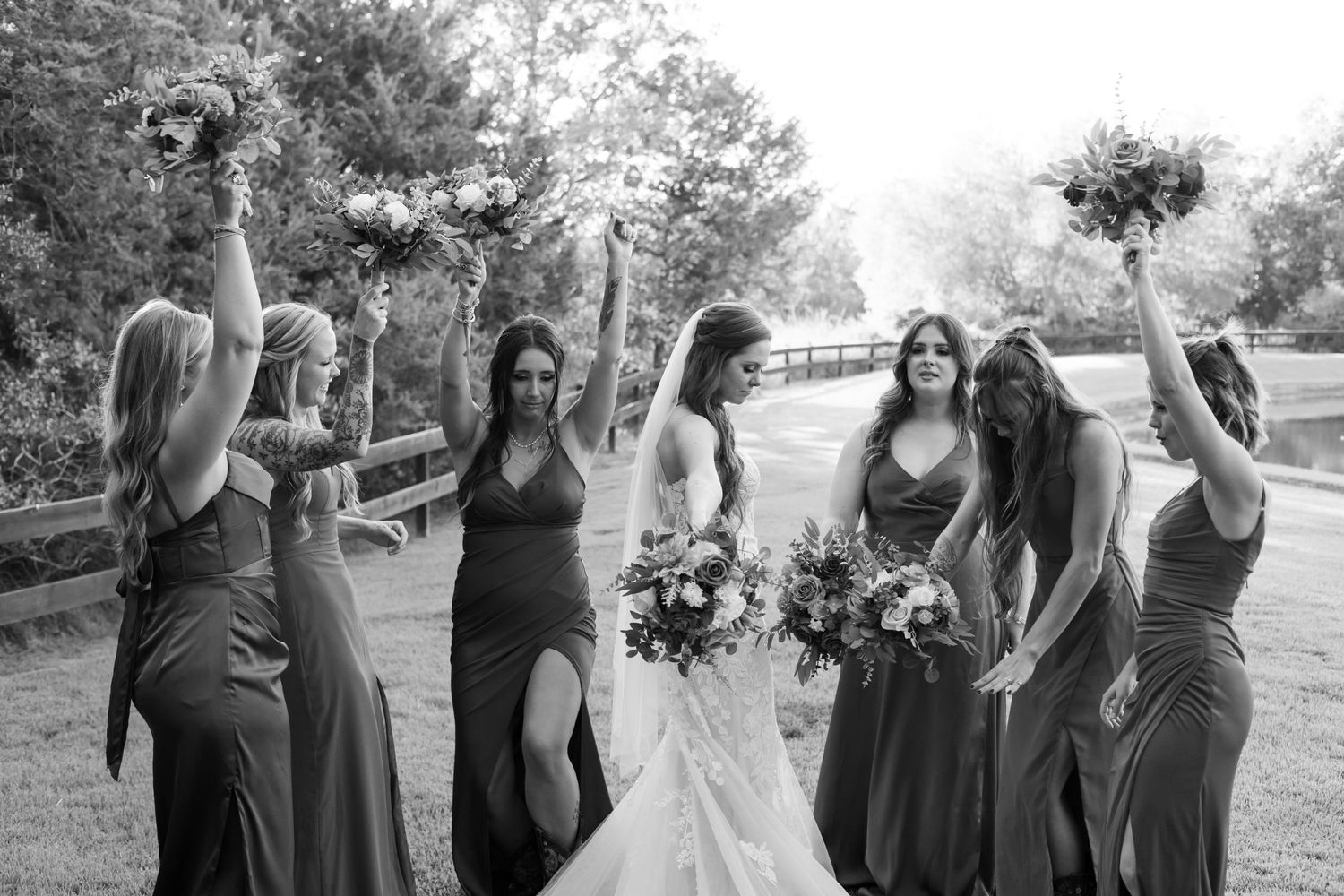 Black and white photo of bridesmaids celebrating with bouquets on a garden path.