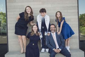 Family of five smiling together outdoors during a Bar Mitzvah celebration, boy in tallit centered.