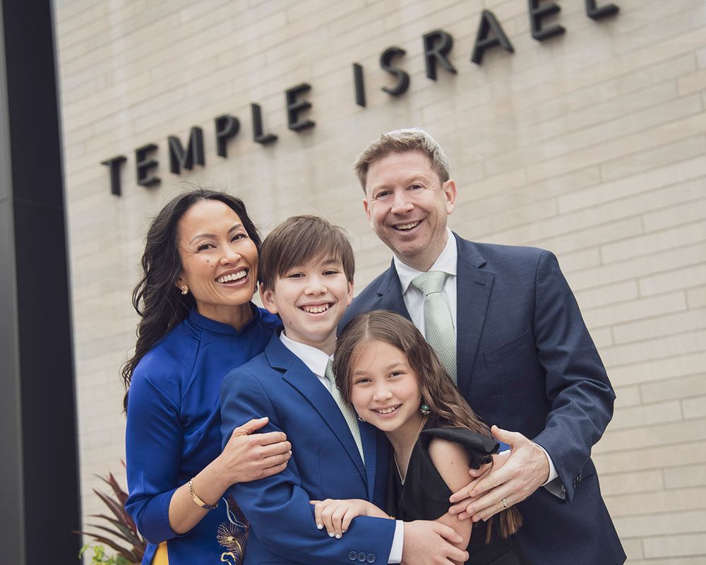 Family of four smiling together outside Temple Israel, dressed in formal attire for a special occasion.