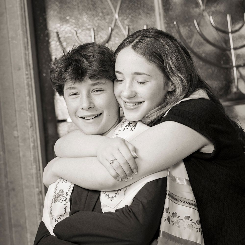Two smiling children share a warm hug in a black and white portrait photo.