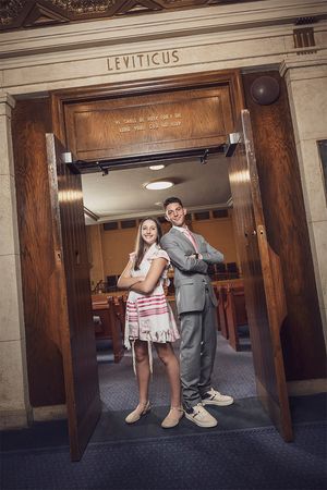 Two teens pose back-to-back in formal attire at a synagogue entrance beneath a Leviticus sign.