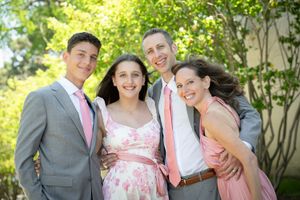 Family of four posing outdoors in pink and gray formal attire, smiling together at a special occasion.
