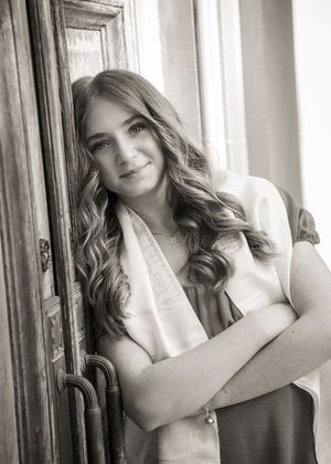 Black and white portrait of someone in a white top leaning against a vintage wooden door.