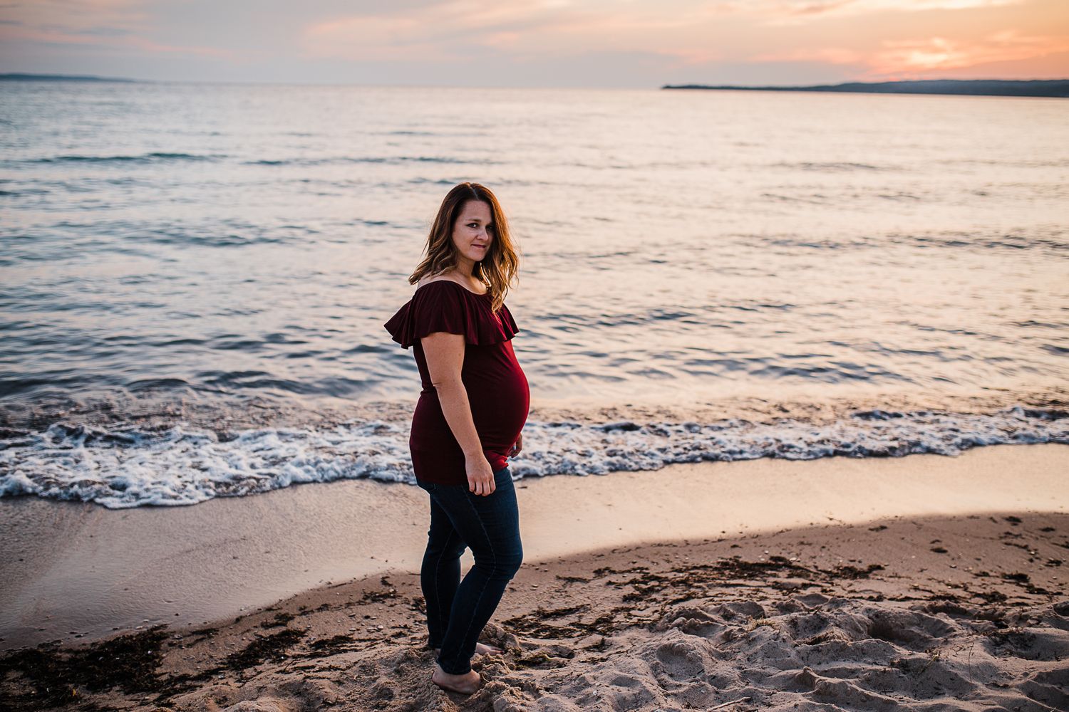 A serene beach maternity portrait during golden hour with gentle waves in the background.