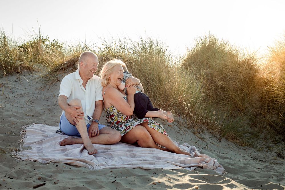 On a beach on Hayling Island, Hampshire, a couple sits in the sand at sunset, arms open as their grandson runs to them.