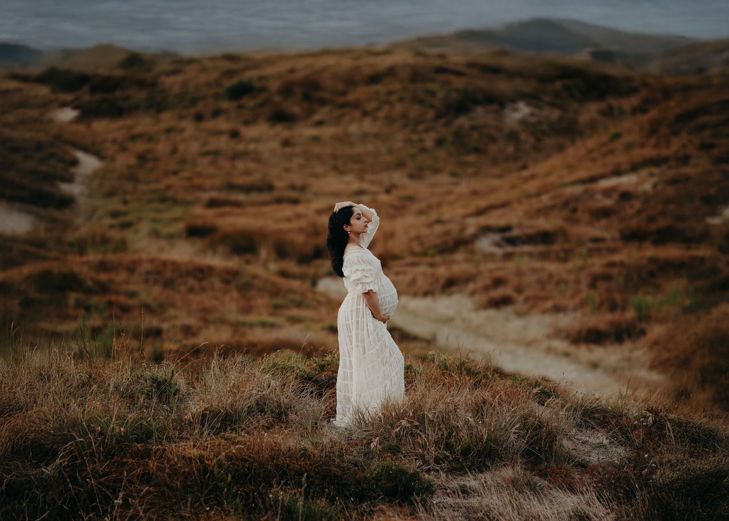 Woman in flowing red dress twirling in golden sunset light on grassy hillside.