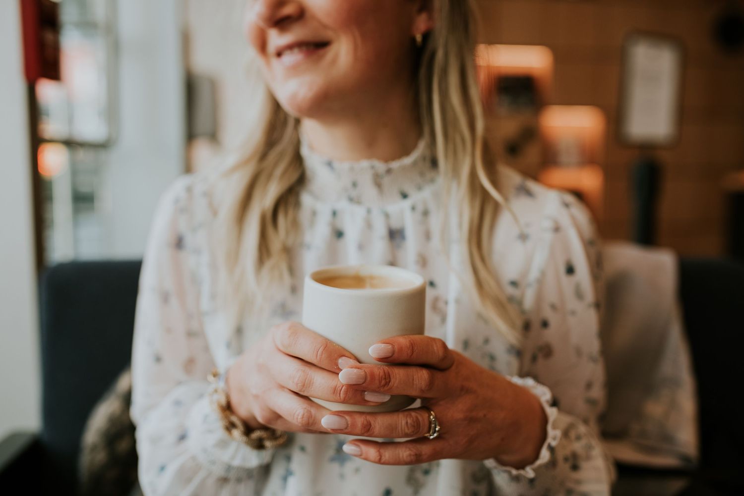 Close-up of a woman holding coffee in a coffee shop, smiling in background.