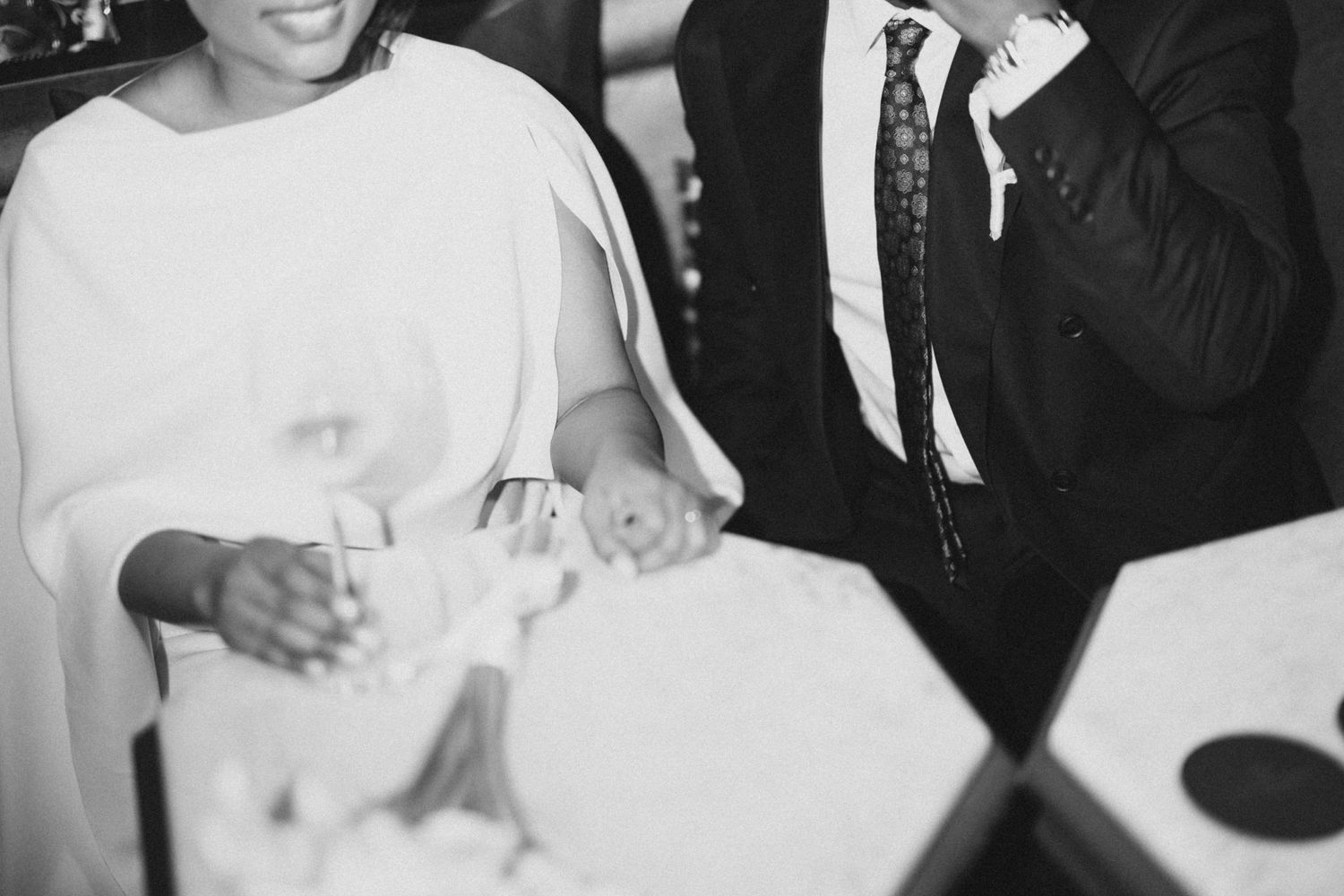 Black and white candid moment showing hands and laughter during a wedding celebration.