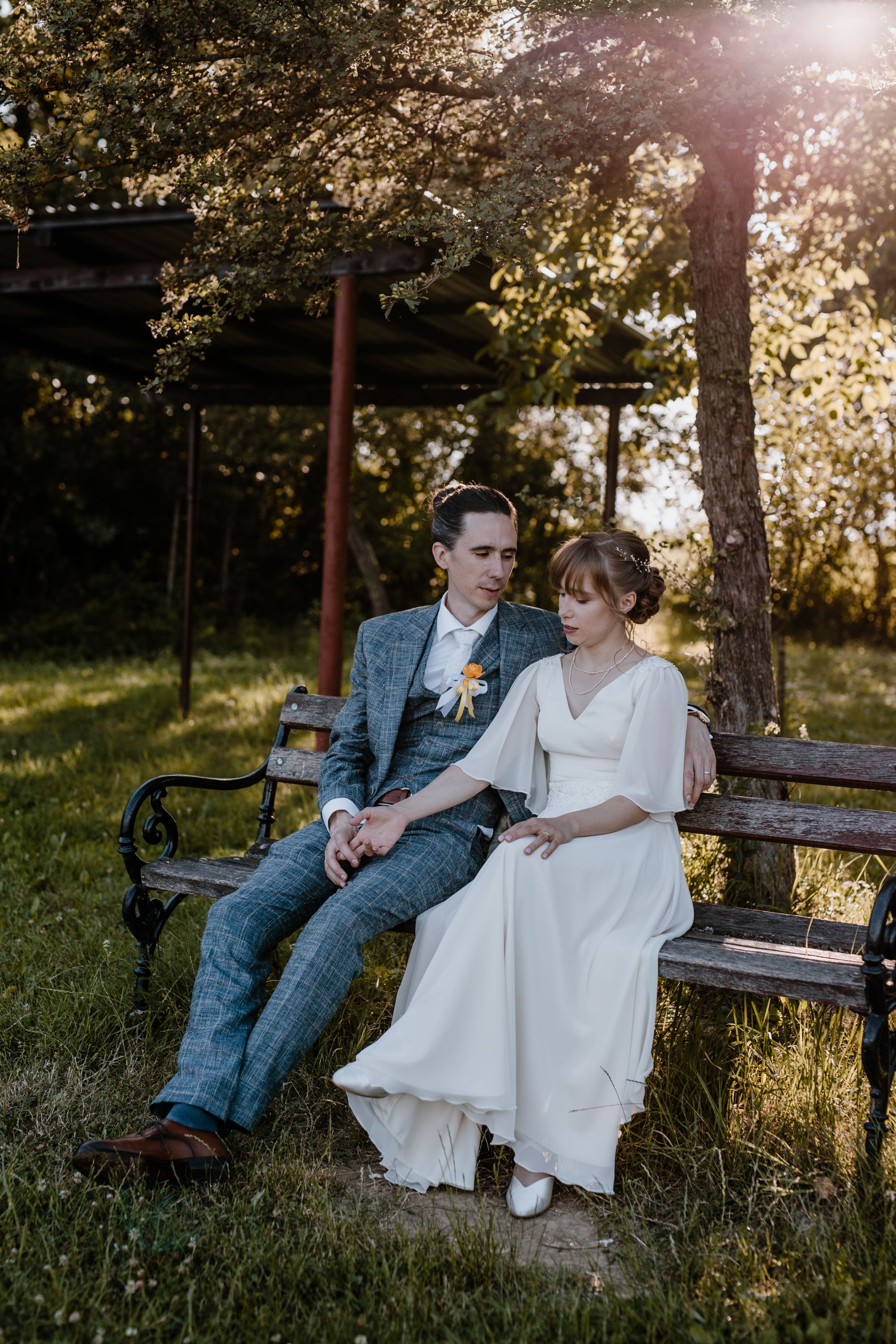 Intimni trenuci mladenaca koji sjede na klupici pored jezera prikazani kroz vjenčanu fotografiju.