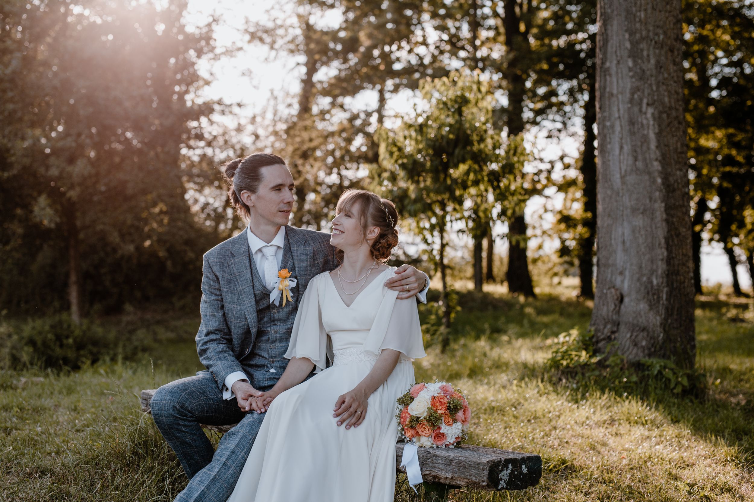 Portret mladenaca koji sjede na klupici dok zlatno sunce prosijava prikazano kroz vjenčanu fotografiju.