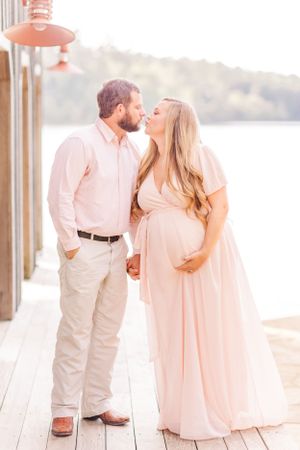 A romantic maternity portrait on a deck with the couple in blush-colored formal wear.