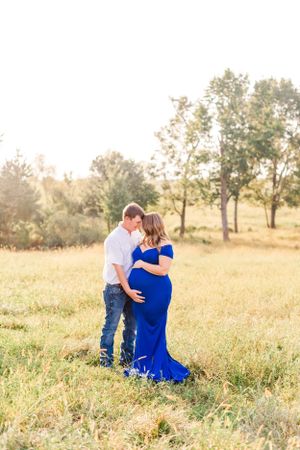 A romantic maternity photo of a couple in an open field at sunset with a flowing blue dress.