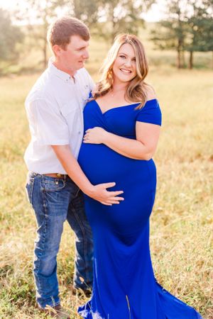 A tender maternity moment captured in golden sunlight with a couple in a grassy field.