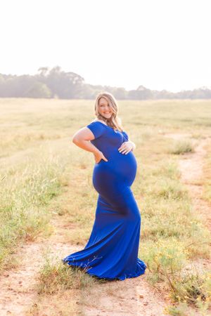 A expectant mother poses in a form-fitting royal blue dress during a sunset maternity photoshoot.
