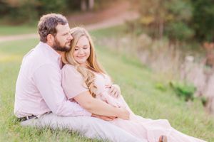 Romantic maternity photo of couple sitting together in a sunlit grassy field.