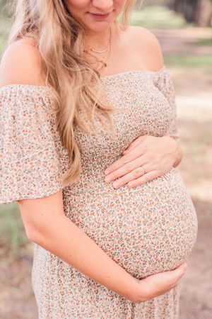 Close-up shot of pregnant belly in a floral off-shoulder dress during outdoor maternity session.