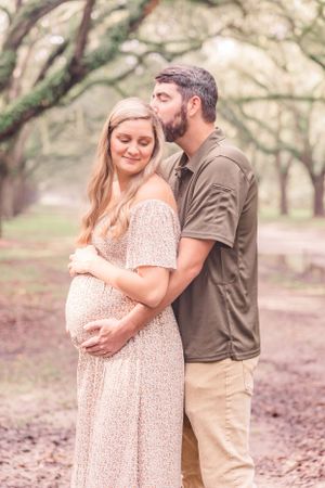 Intimate maternity portrait under Spanish moss-draped trees showing tender moment between couple.