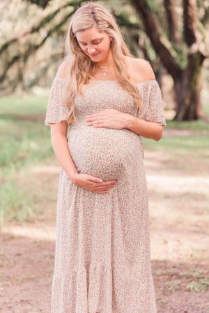 Serene maternity portrait of expectant mother holding bump in floral maxi dress outdoors.