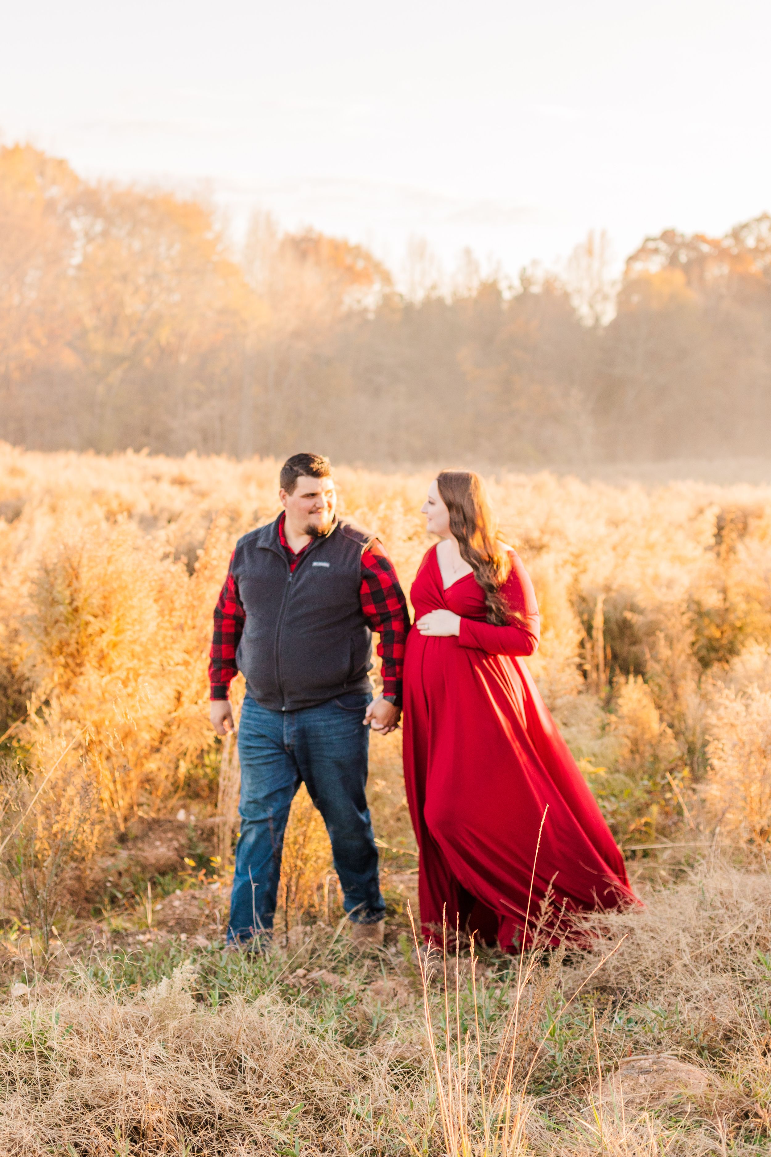 Expecting couple standing in autumn field at golden hour wearing red dress and plaid shirt.