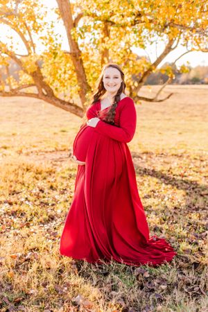 Maternity photo featuring red dress against fall foliage backdrop.
