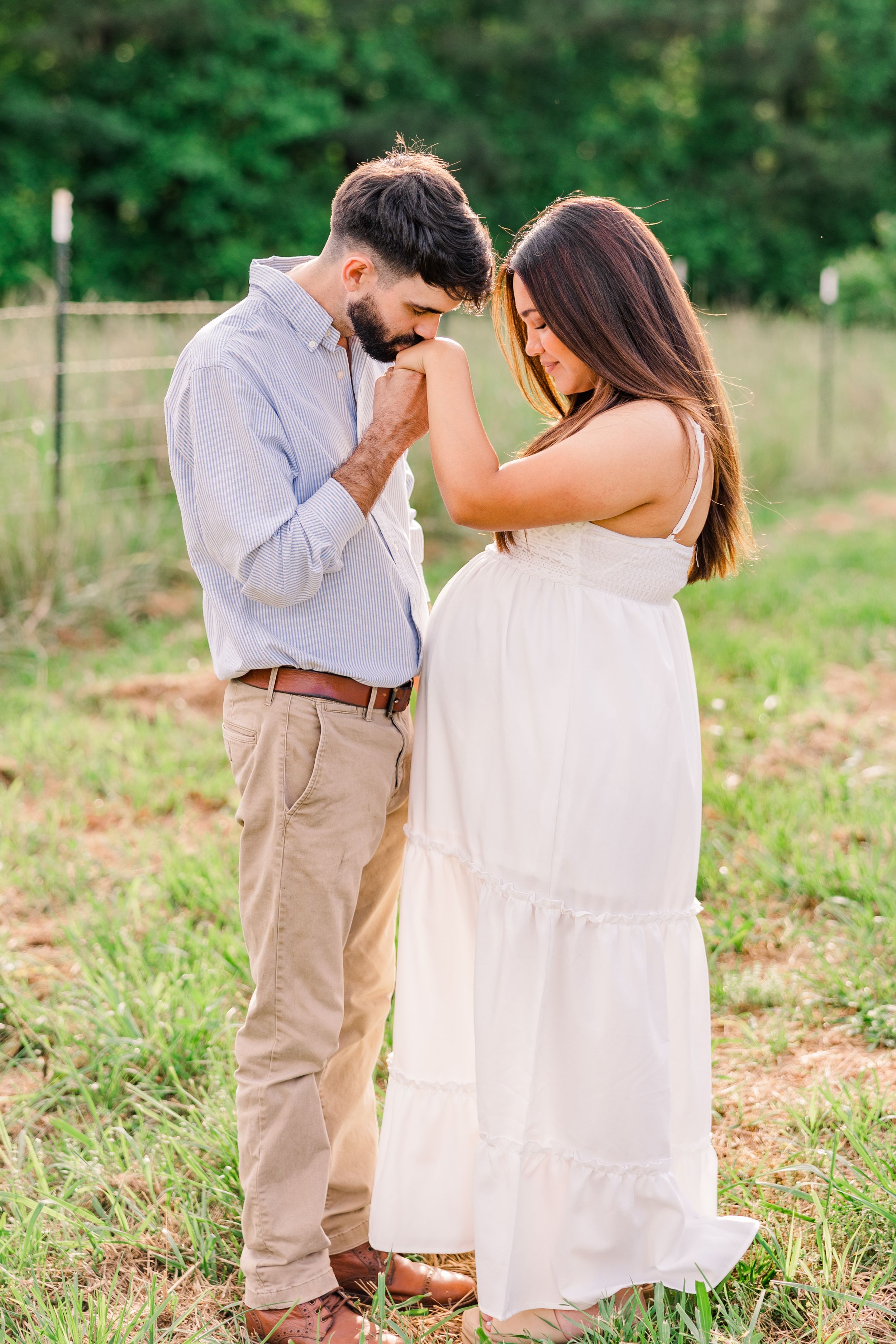 Romantic maternity moment captured as couple stands together in grassy field.