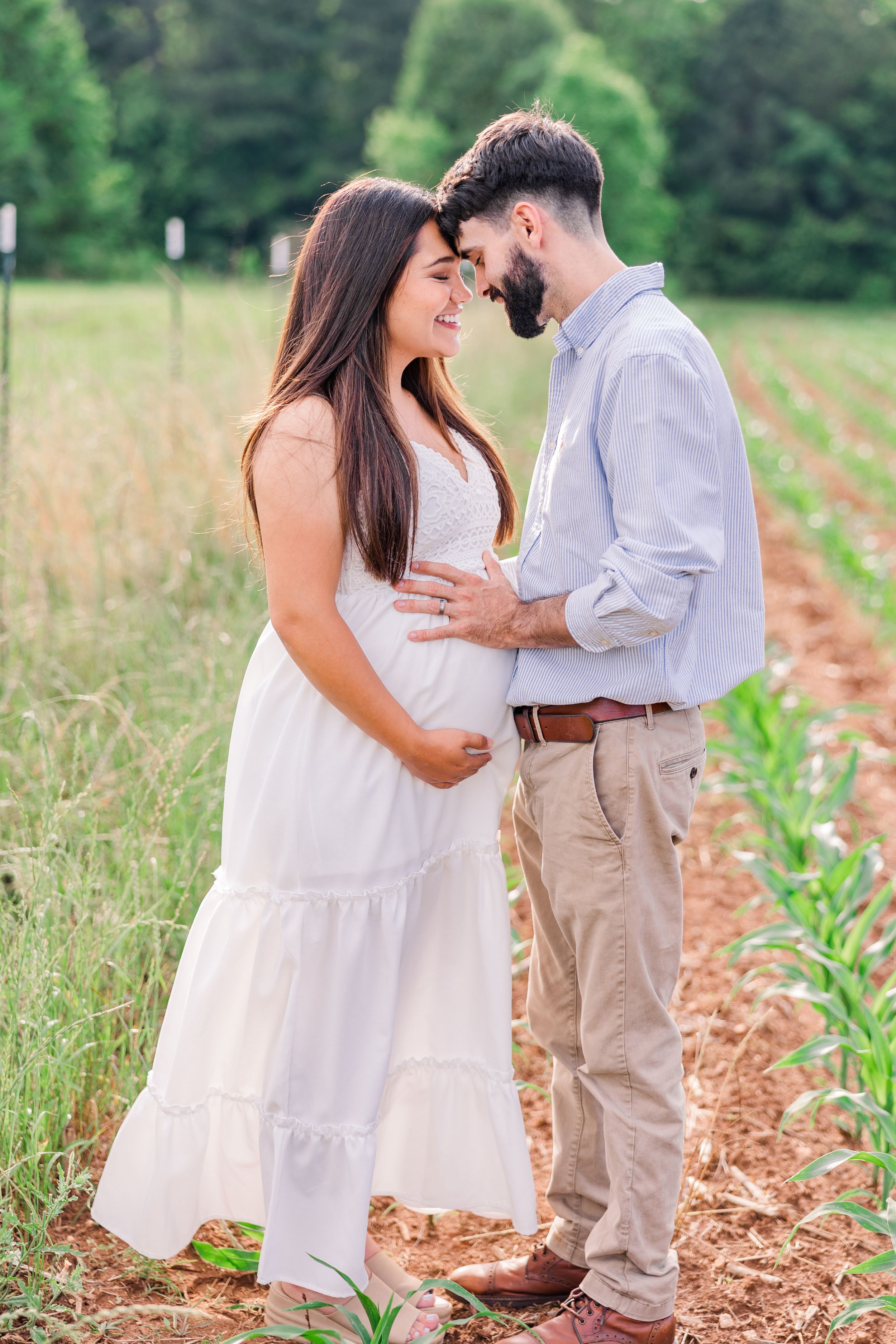 Intimate maternity photo of a couple in white and khaki standing in a rustic field.