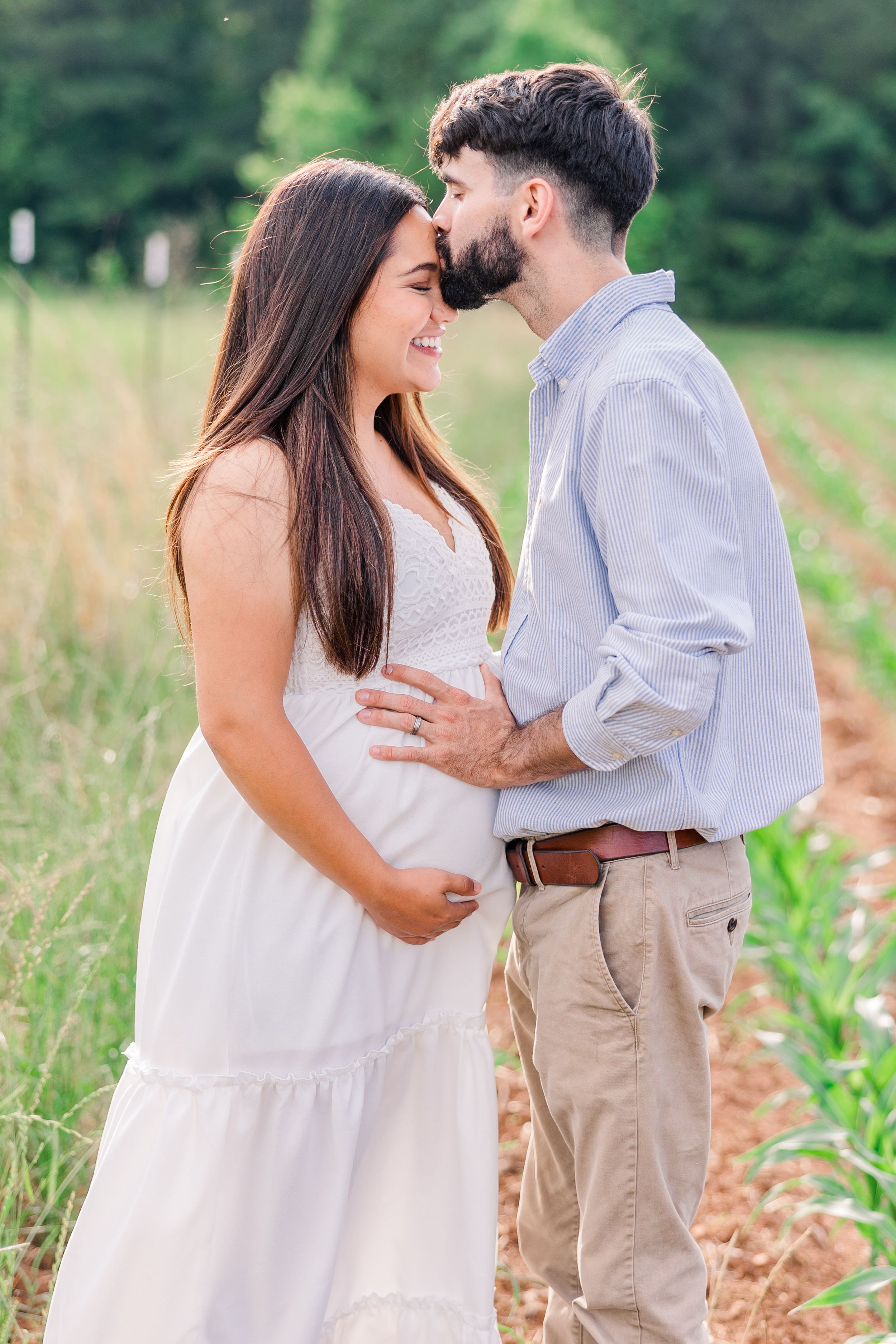 Romantic maternity portrait of a couple sharing a tender moment in a summer field.