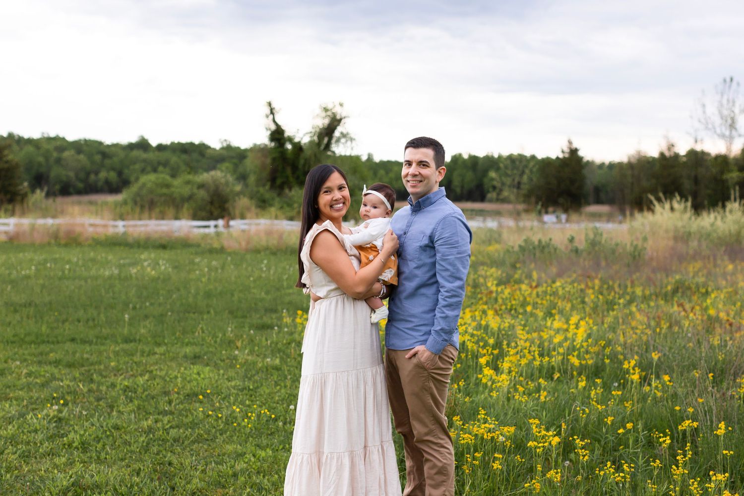 A couple stands lovingly in a meadow with yellow wildflowers and trees in the background.
